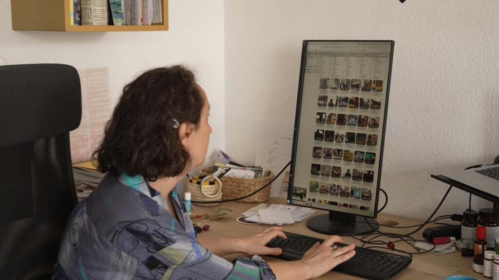 a white Person with brown hair sits in front of an upright screen with thumpnails on it